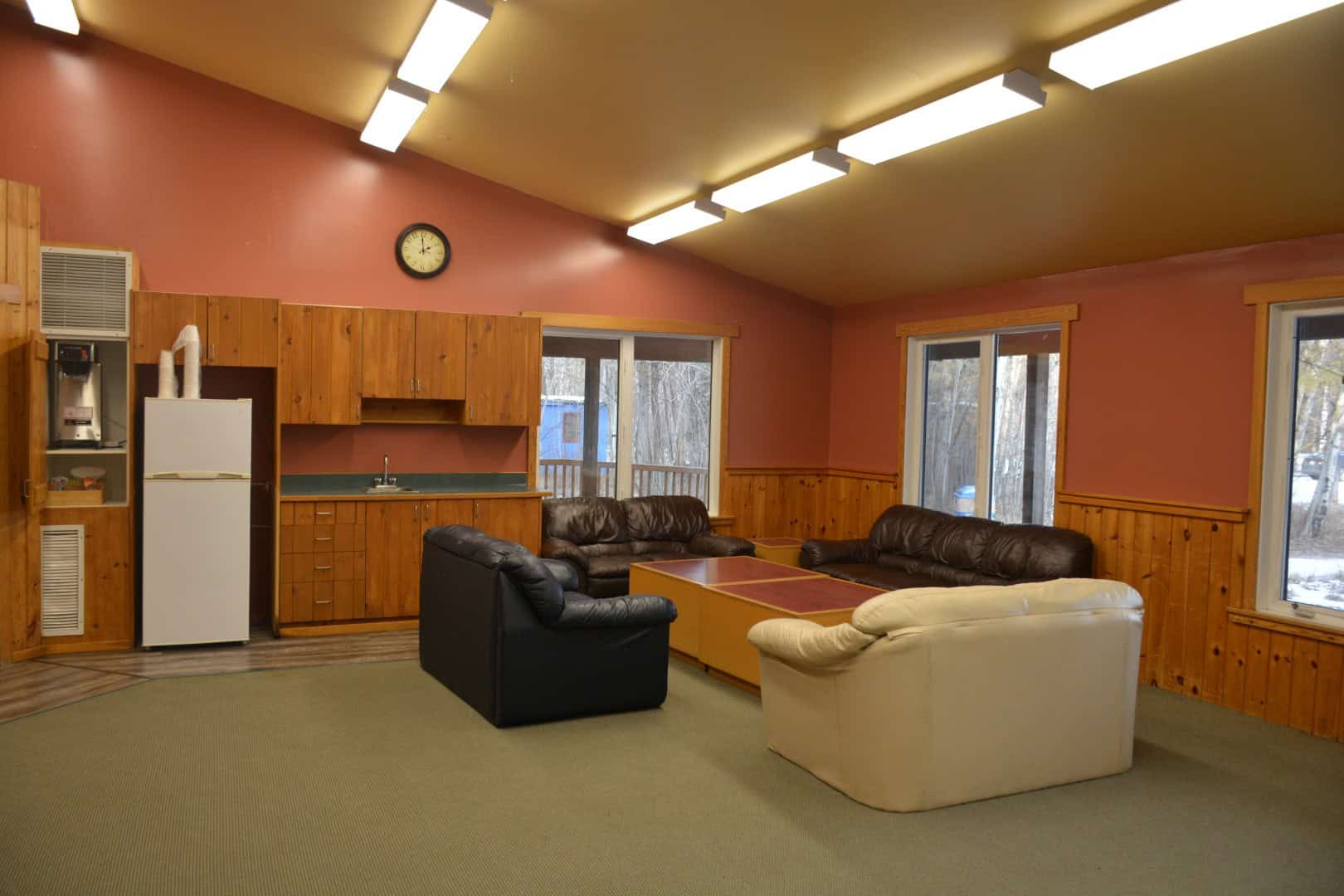 Cozy indoor lodge at Camp Arnes with leather sofas, wooden accents, large windows, and warm lighting, ideal for family gatherings and relaxation in a scenic outdoor setting.
