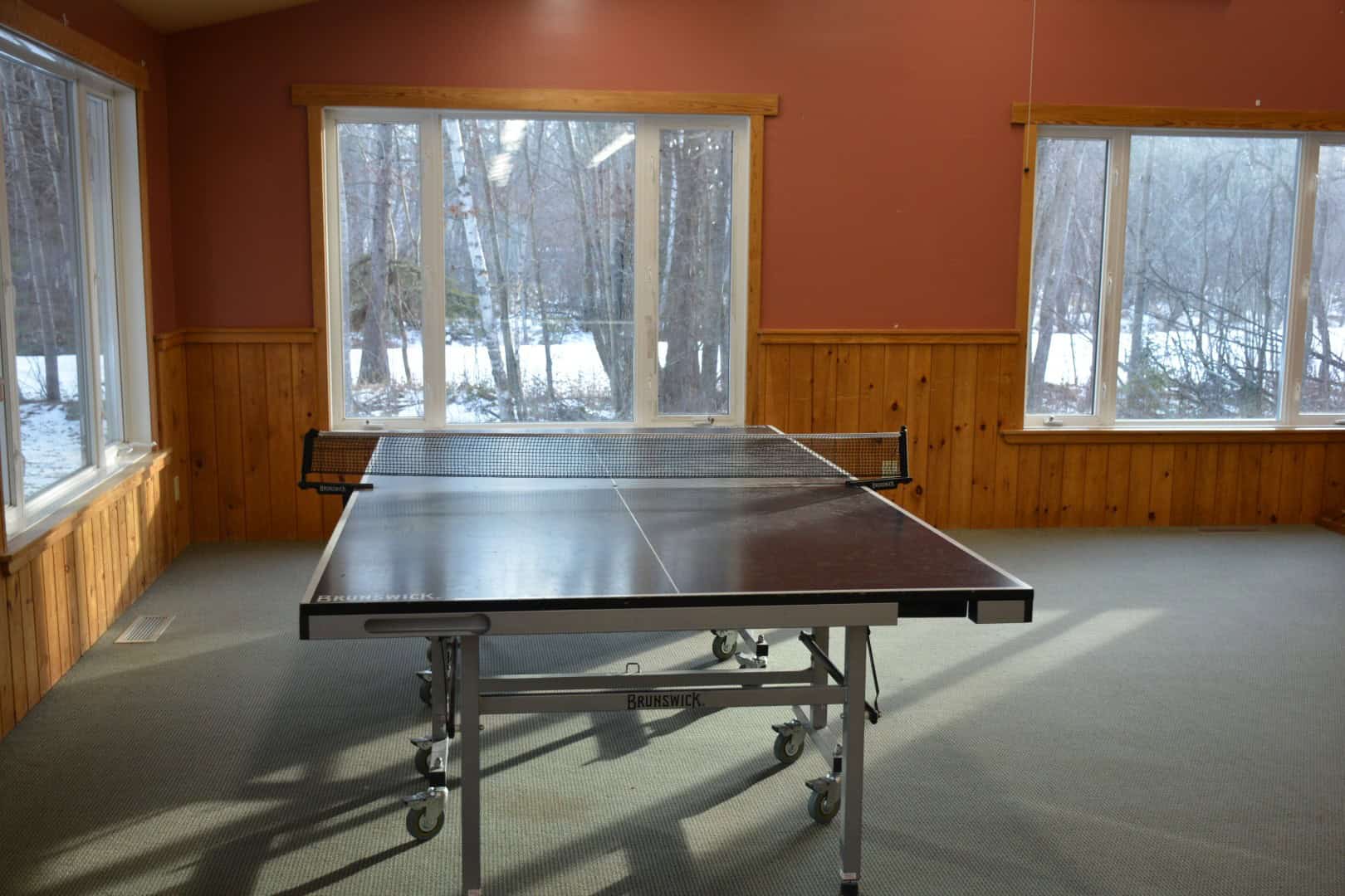 Indoor table tennis room at Camp Arnes with large windows overlooking a snowy outdoor landscape.