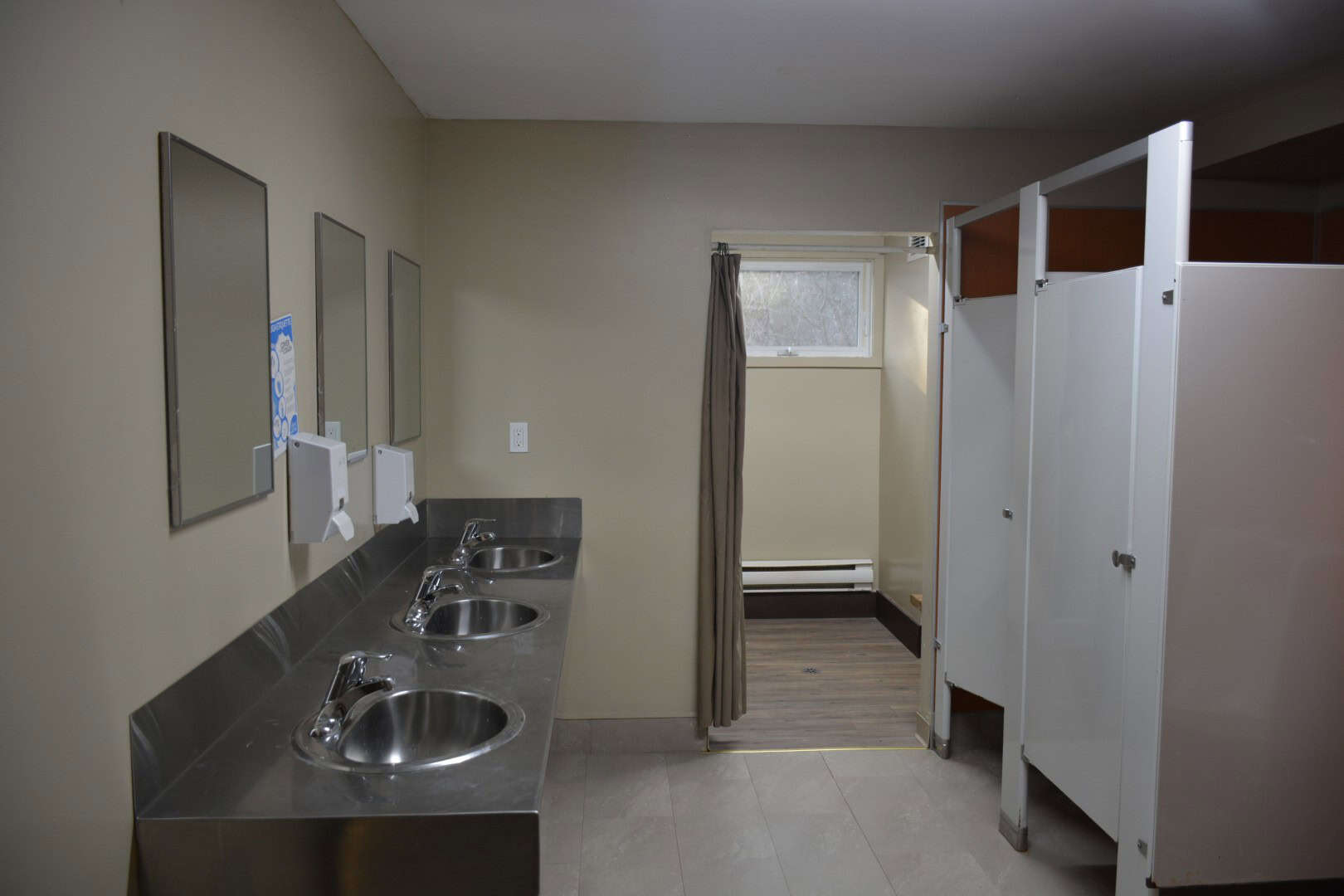 Clean communal bathroom with stainless steel sinks, mirrors, soap dispensers, and a small window at Camp Arnes for camping and outdoor adventures.