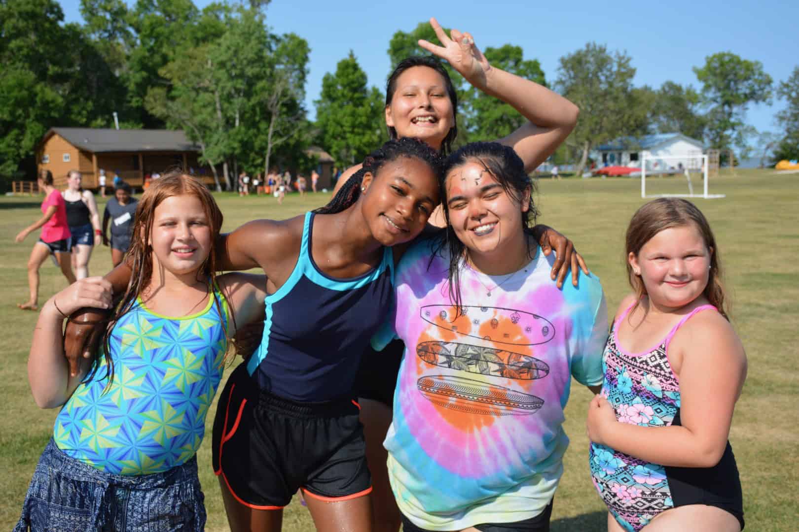 Vibrant group of young girls enjoying outdoor activities at Camp Arnes summer camp, showcasing friendship, fun, and outdoor adventure on lush green fields.