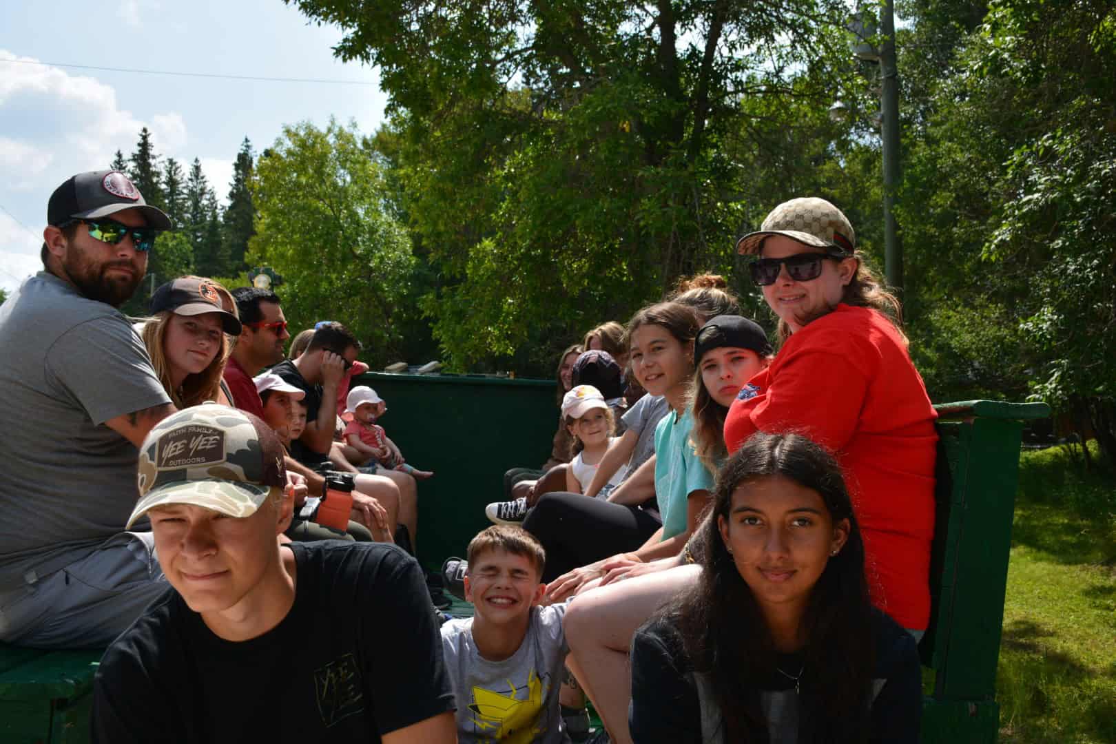 Kids and counselors enjoying a scenic outdoor train ride at Camp Arnes in a lush, green environment with bright blue skies.