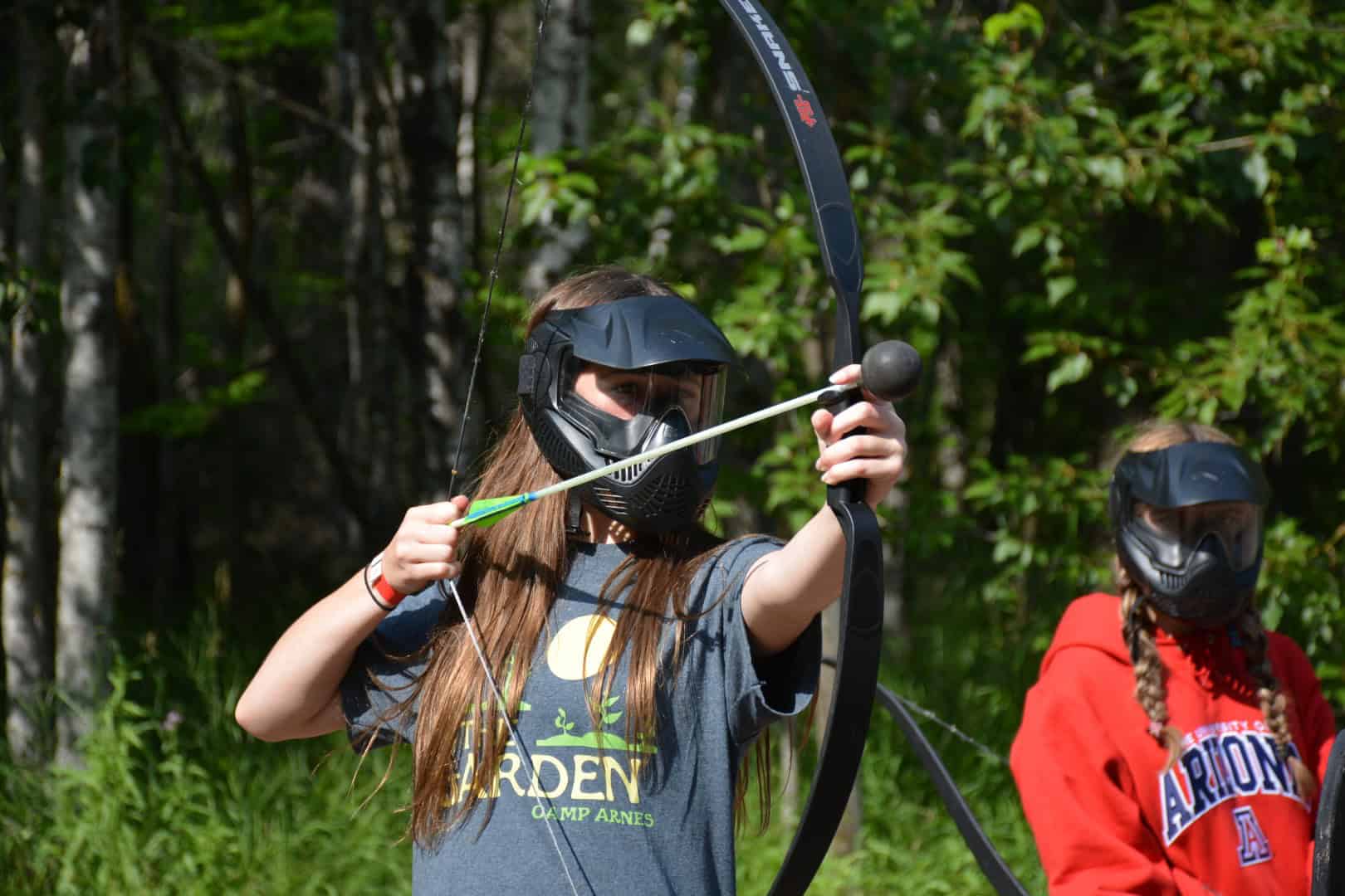 Kids enjoying archery at Camp Arnes outdoor adventure activities in a lush forest setting.