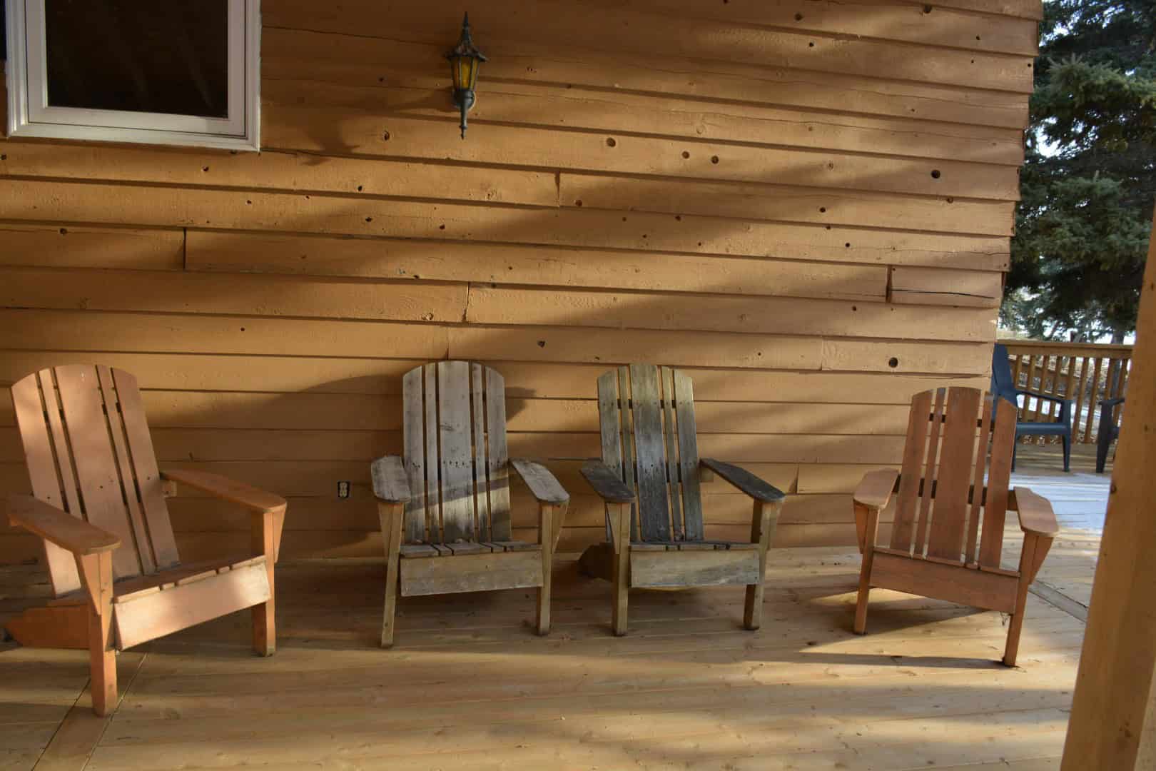 Adirondack chairs on a wooden deck against a log cabin wall at Camp Arnes, Manitoba, showcasing outdoor relaxation and rustic accommodations.
