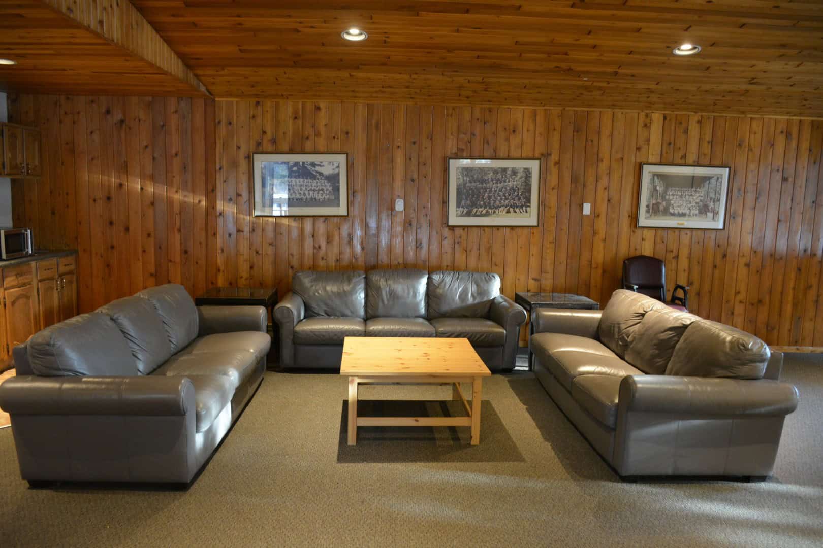 Comfortable indoor lounge area at Camp Arnes with leather sofas, wooden walls, and framed decor, offering a cozy space for relaxation during camping trips in Manitoba.