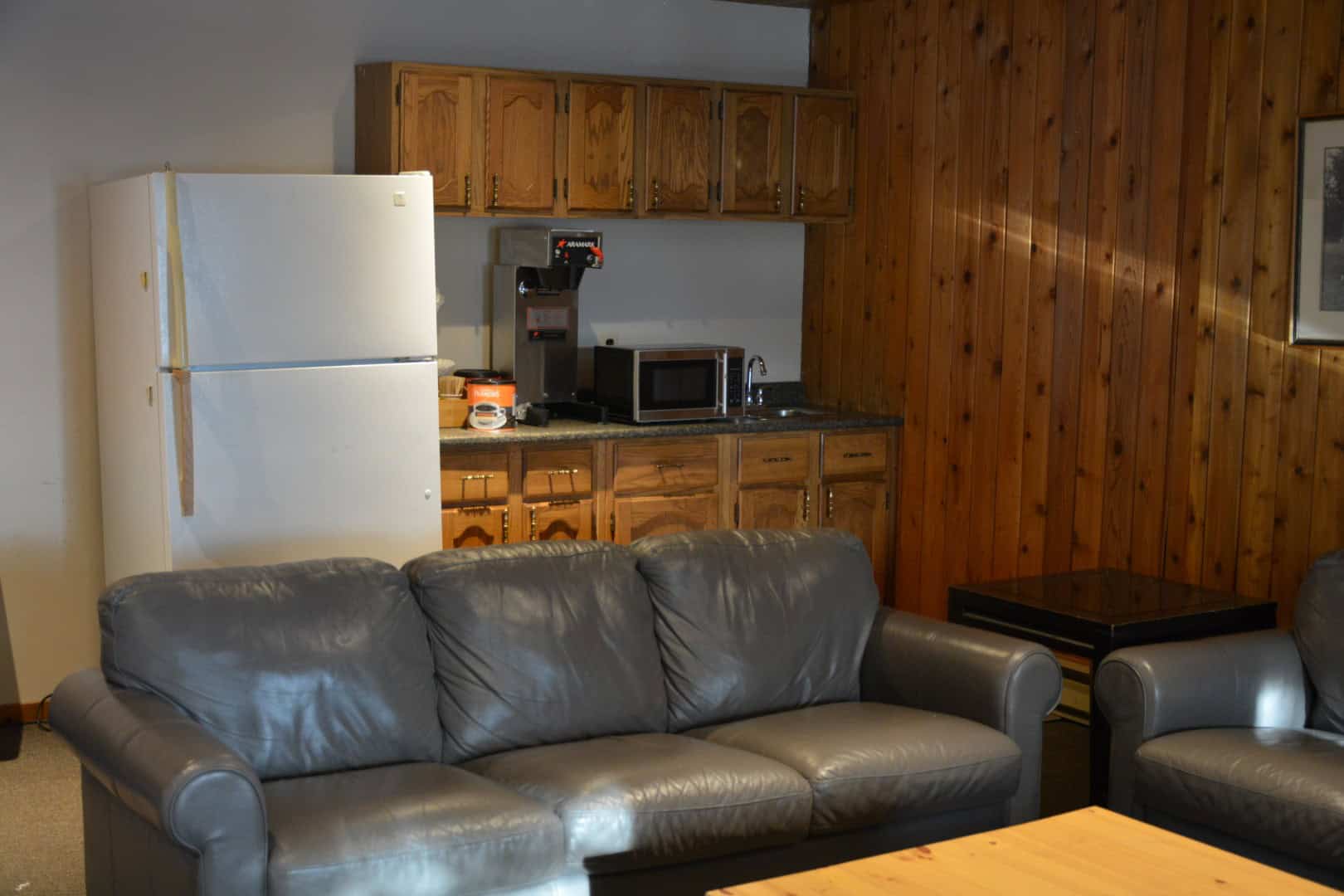 Cozy interior of Camp Arnes with a living area and kitchenette, featuring wooden walls, leather sofas, and essential appliances, perfect for a relaxing escape in a scenic outdoor setting.