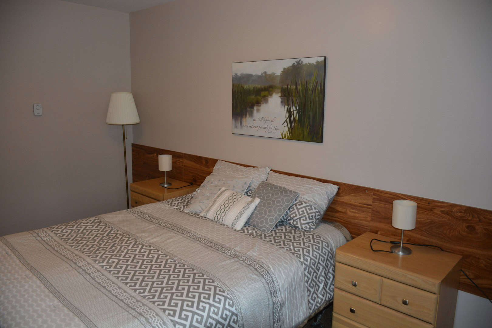 Cozy bedroom at Camp Arnes with a queen-sized bed, modern bedding, wooden headboard, and matching bedside tables featuring lamps, offering a relaxing and comfortable lodging experience.