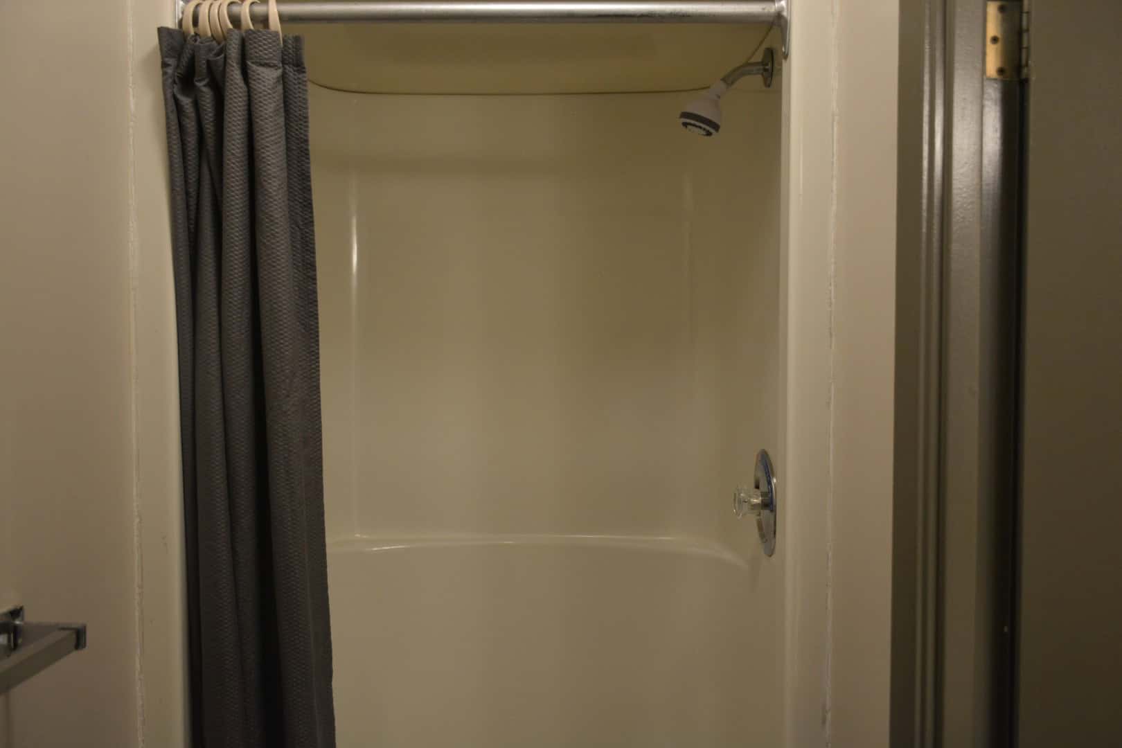 Shower stall at Camp Arnes campground with shower curtain and fixtures in a cozy camping cabin or restroom facility.