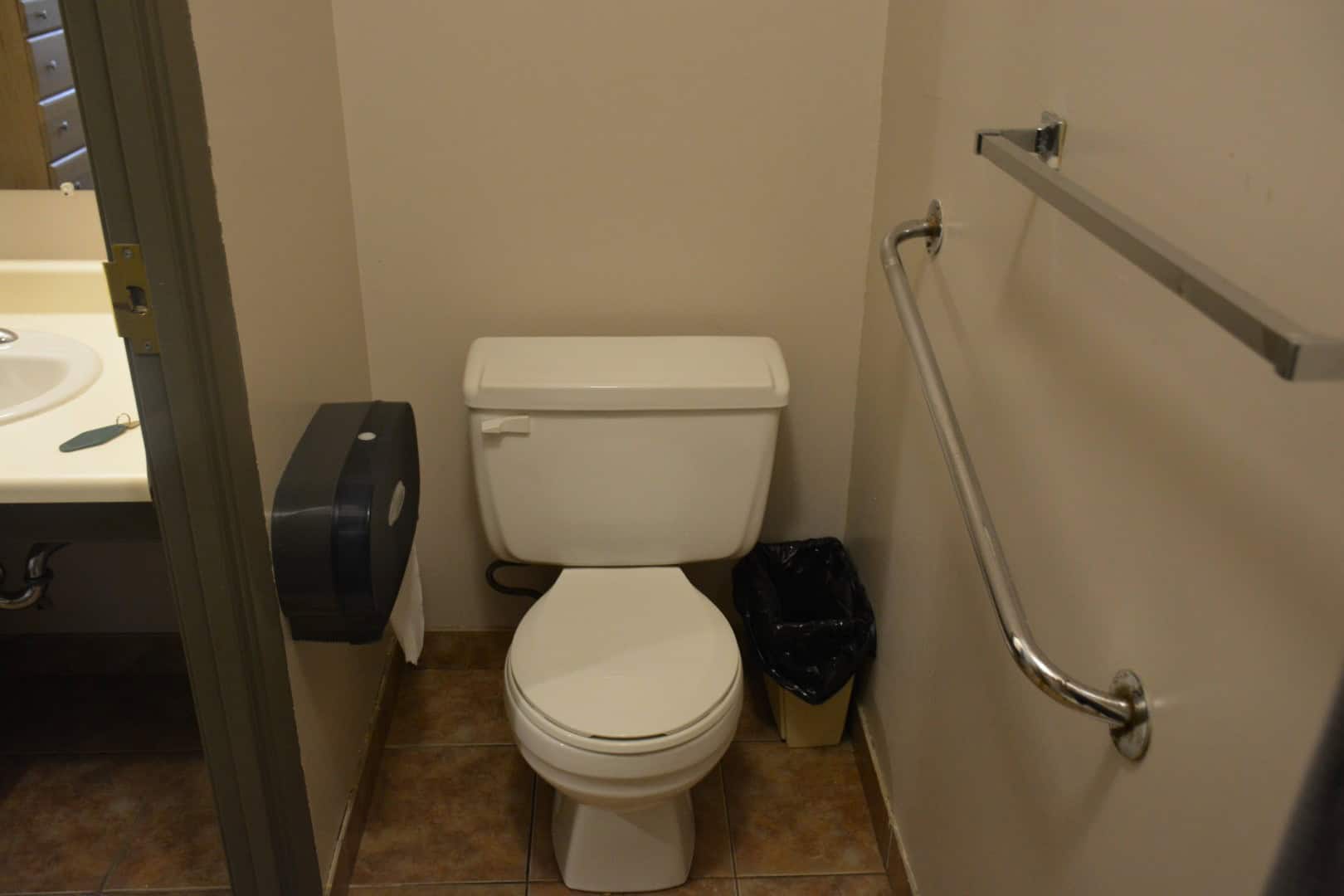 Toilet with grab bar and trash bin in indoor restroom at Camp Arnes, a lakeside retreat and outdoor adventure camp in Manitoba offering family cabins, outdoor activities, and scenic views.
