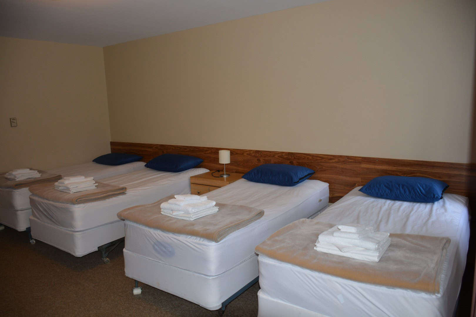 Clean, cozy guest bedroom with four beds featuring white linens, blue pillows, and neatly folded towels at Camp Arnes, a premier outdoor camping and retreat destination in Manitoba.