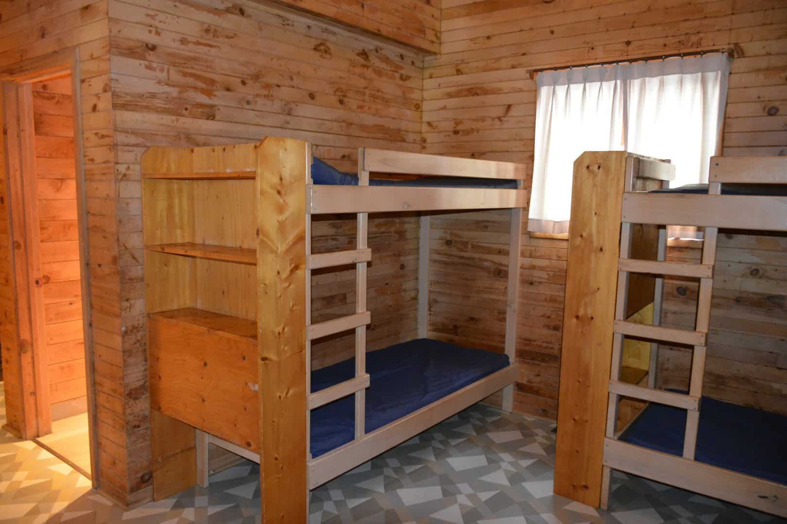 Warm wooden cabin interior with rustic bunk beds at Camp Arnes, featuring natural wood walls, cozy atmosphere, and comfortable sleeping arrangements for a memorable outdoor camping experience.