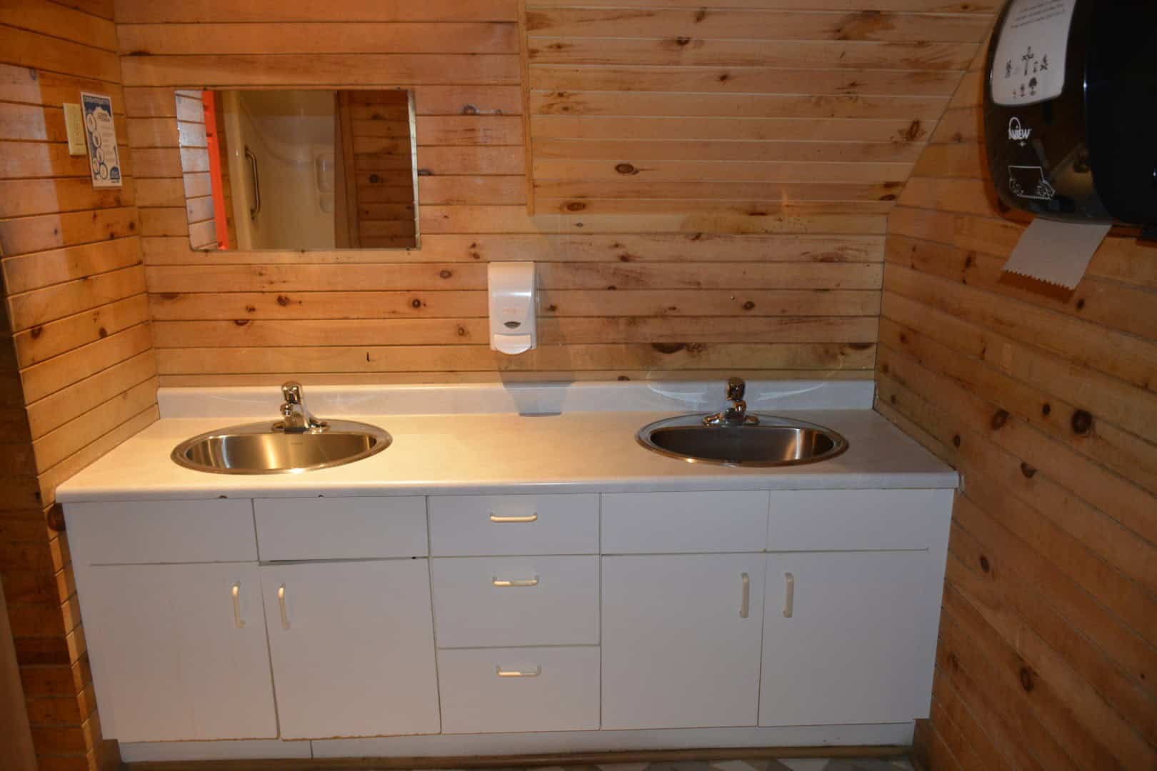 Clean indoor kitchenette with double stainless steel sinks, wooden panel walls, and white cabinetry at Camp Arnes outdoor adventure resort.