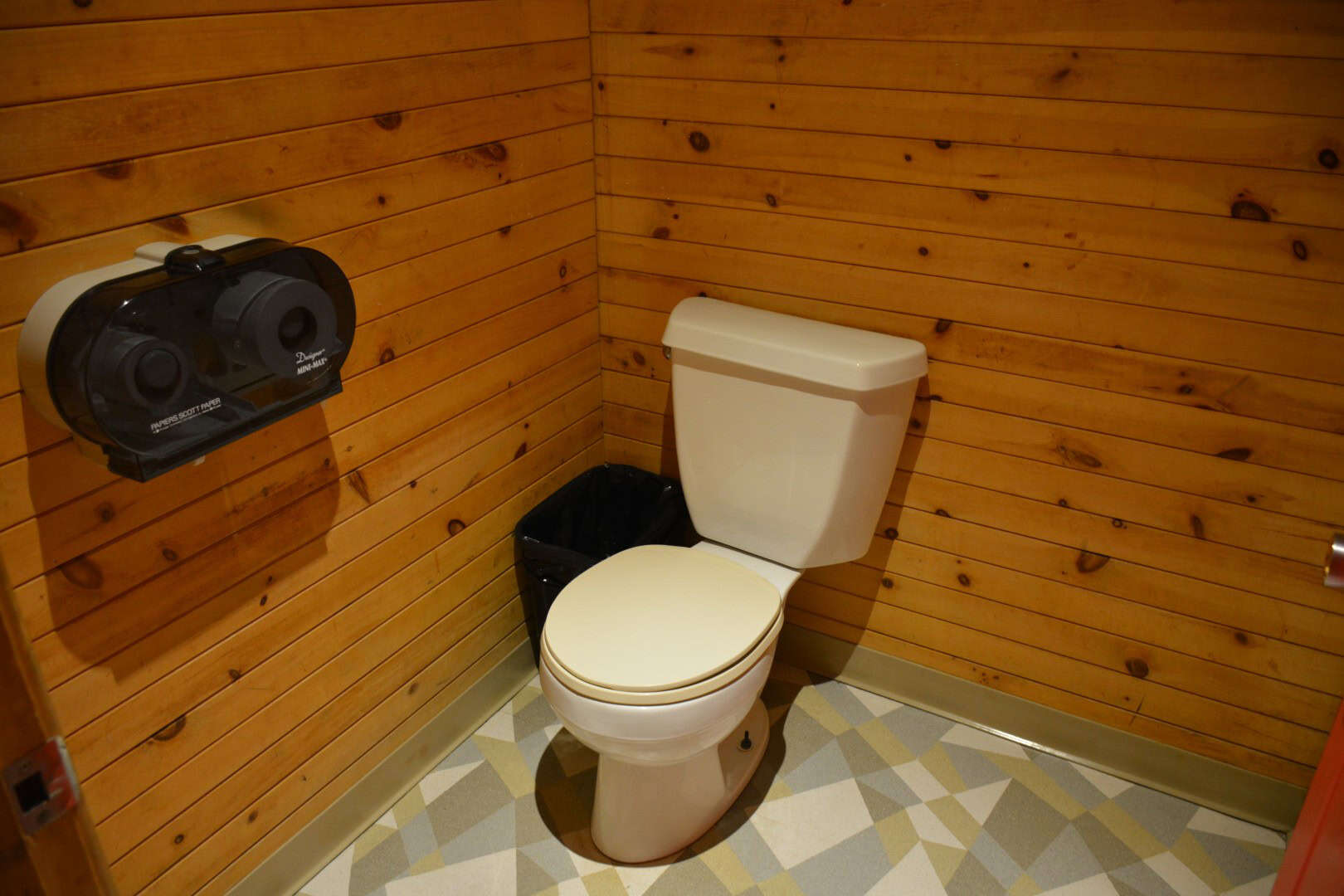 Clean wooden-walled camp restroom with a white toilet and black waste bin at Camp Arnes.