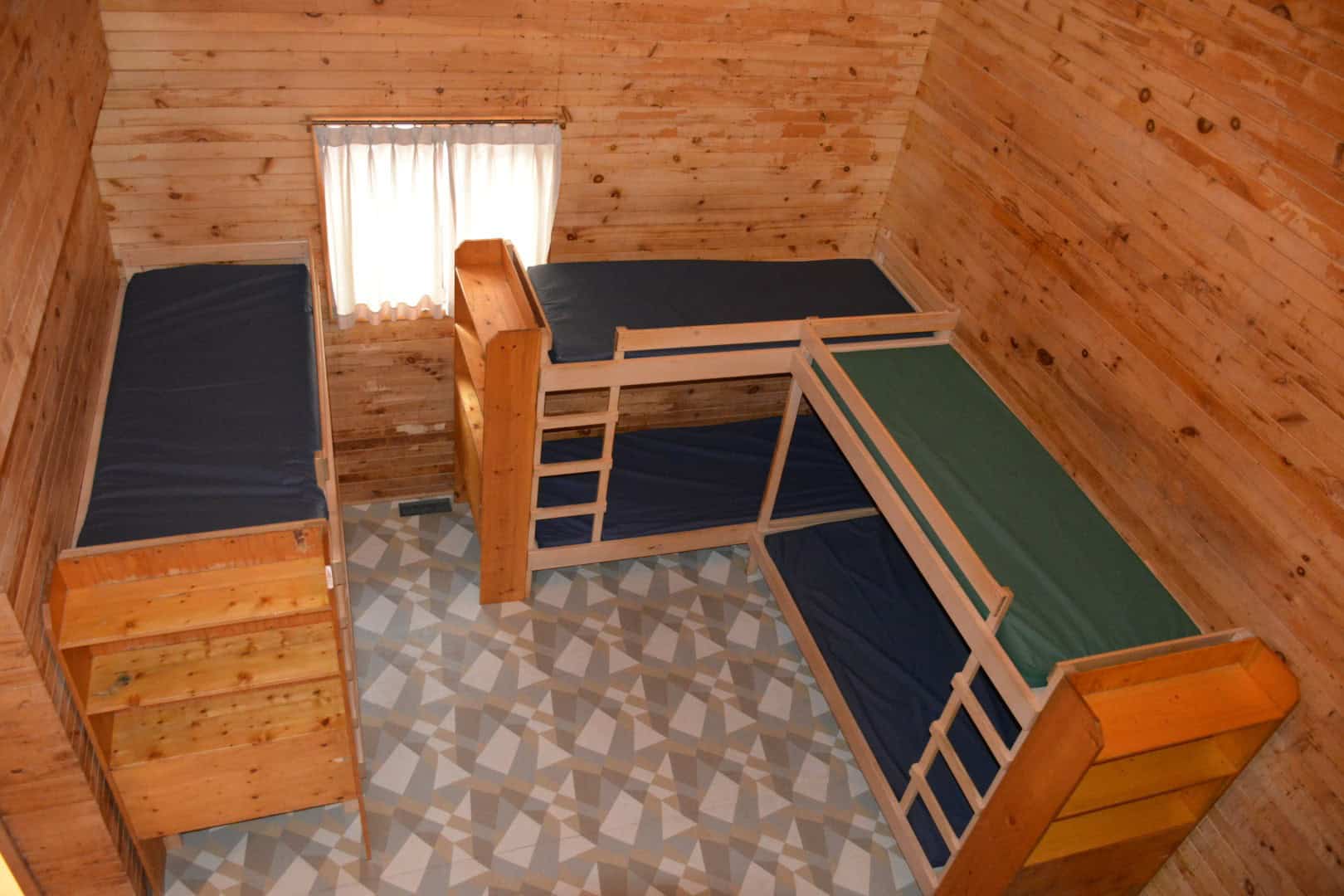 Cozy wooden bunk bed room at Camp Arnes, featuring rustic log bed frames, simple bedding, and natural wood-paneled walls, ideal for a comfortable outdoor camping experience.