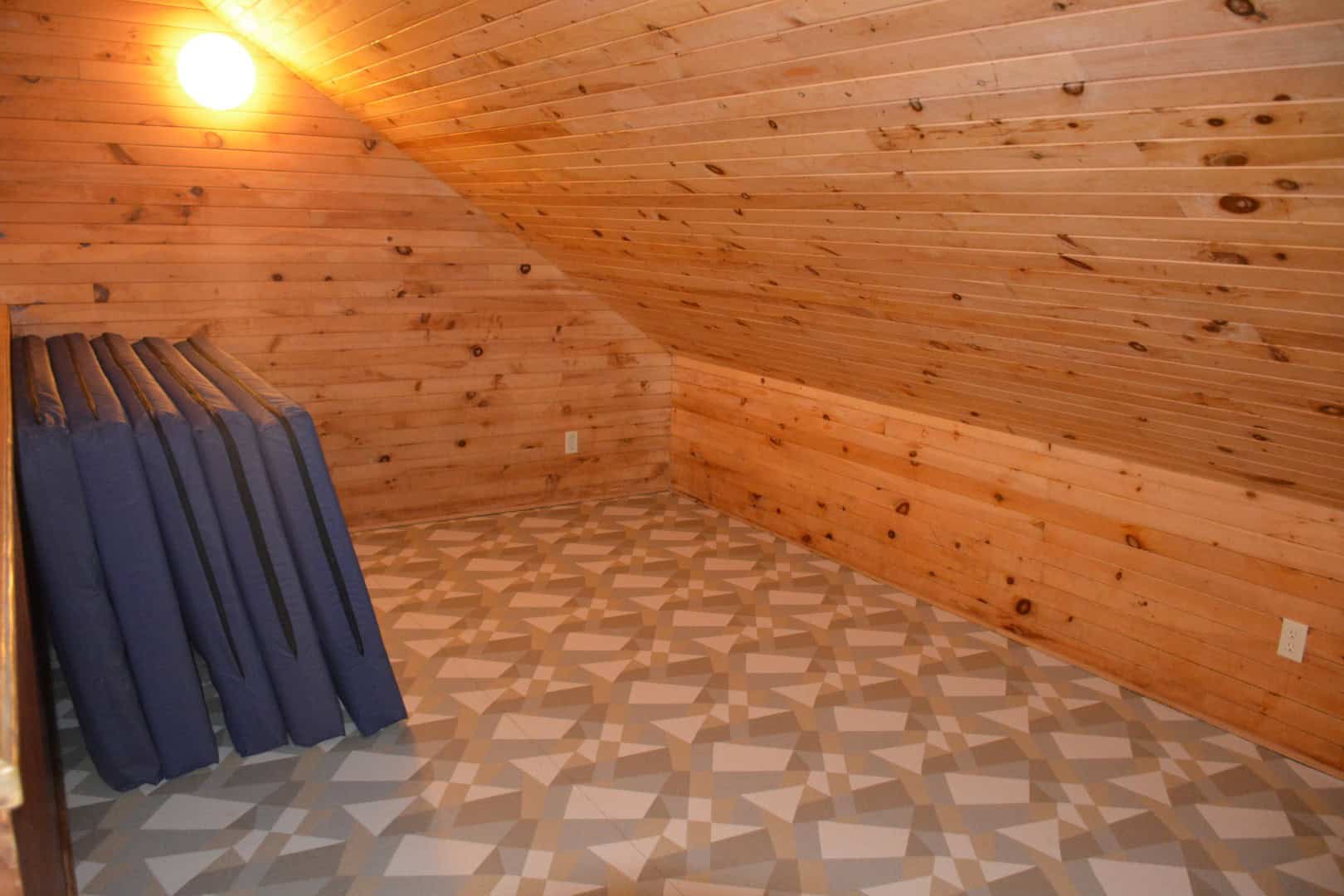 Cozy wooden attic room with sloped pine paneling and patterned vinyl flooring, ideal for relaxation and small gatherings at Camp Arnes.
