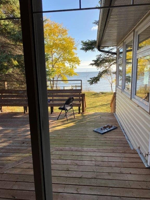 Cozy outdoor deck with lake view, surrounded by trees, at Camp Arnes in Manitoba, offering peaceful scenery, relaxing atmosphere, and direct access to nature for campers and visitors.