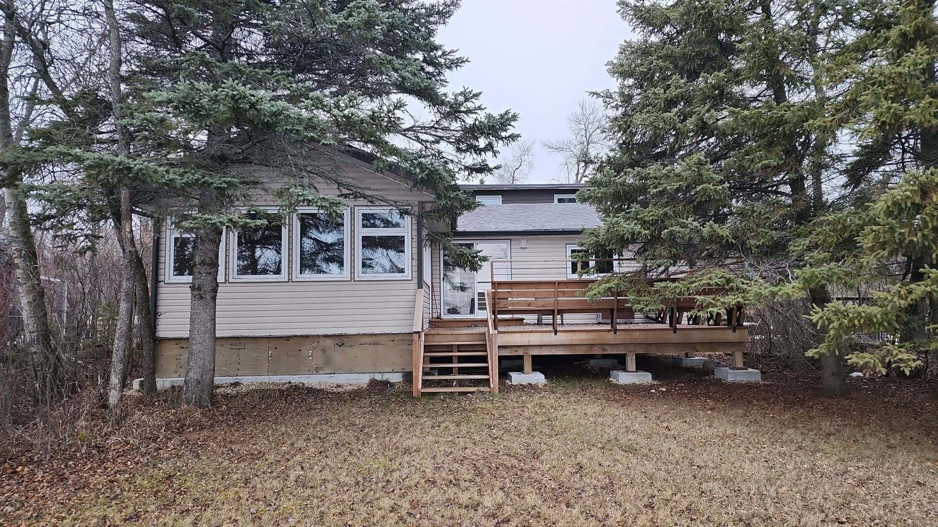 Cozy residential house with a wooden deck, surrounded by tall evergreen trees, in a wooded setting at Camp Arnes. Perfect retreat with natural scenery and outdoor space for relaxation.