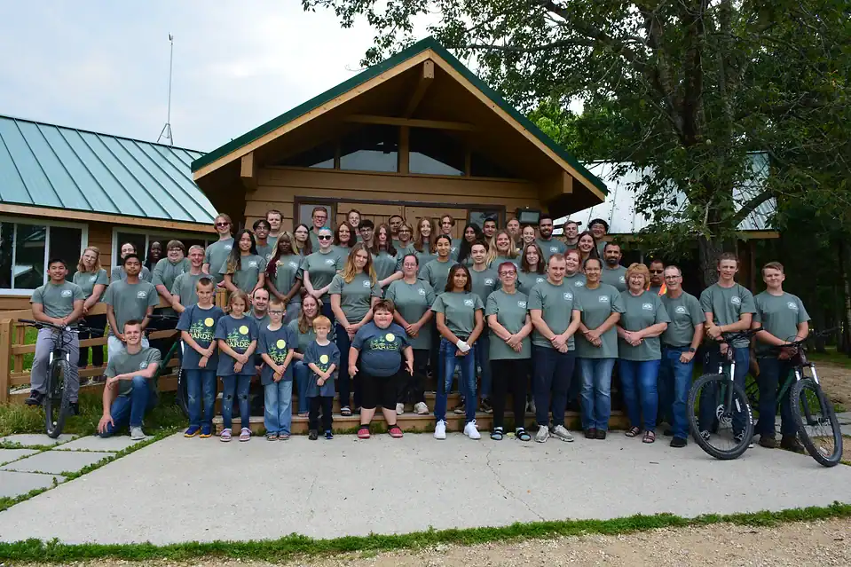 Camp Arnes group photo of staff and campers outside wooden lodge on a sunny day.