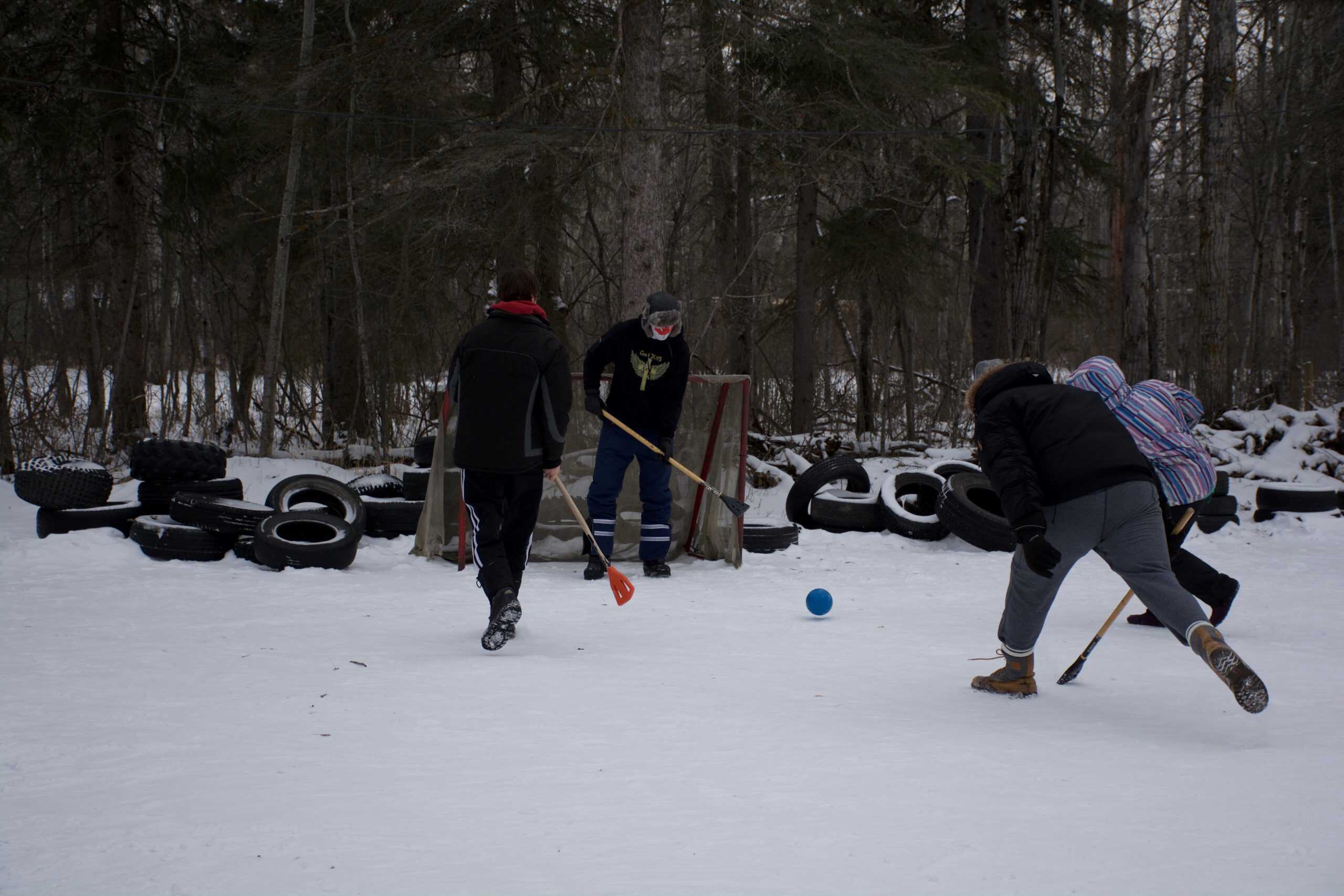 Kids playing ice hockey on snowy outdoor rink at Camp Arnes, Manitoba. Enjoy winter sports and outdoor activities at this family-friendly camp with natural forest scenery and snow-covered grounds.