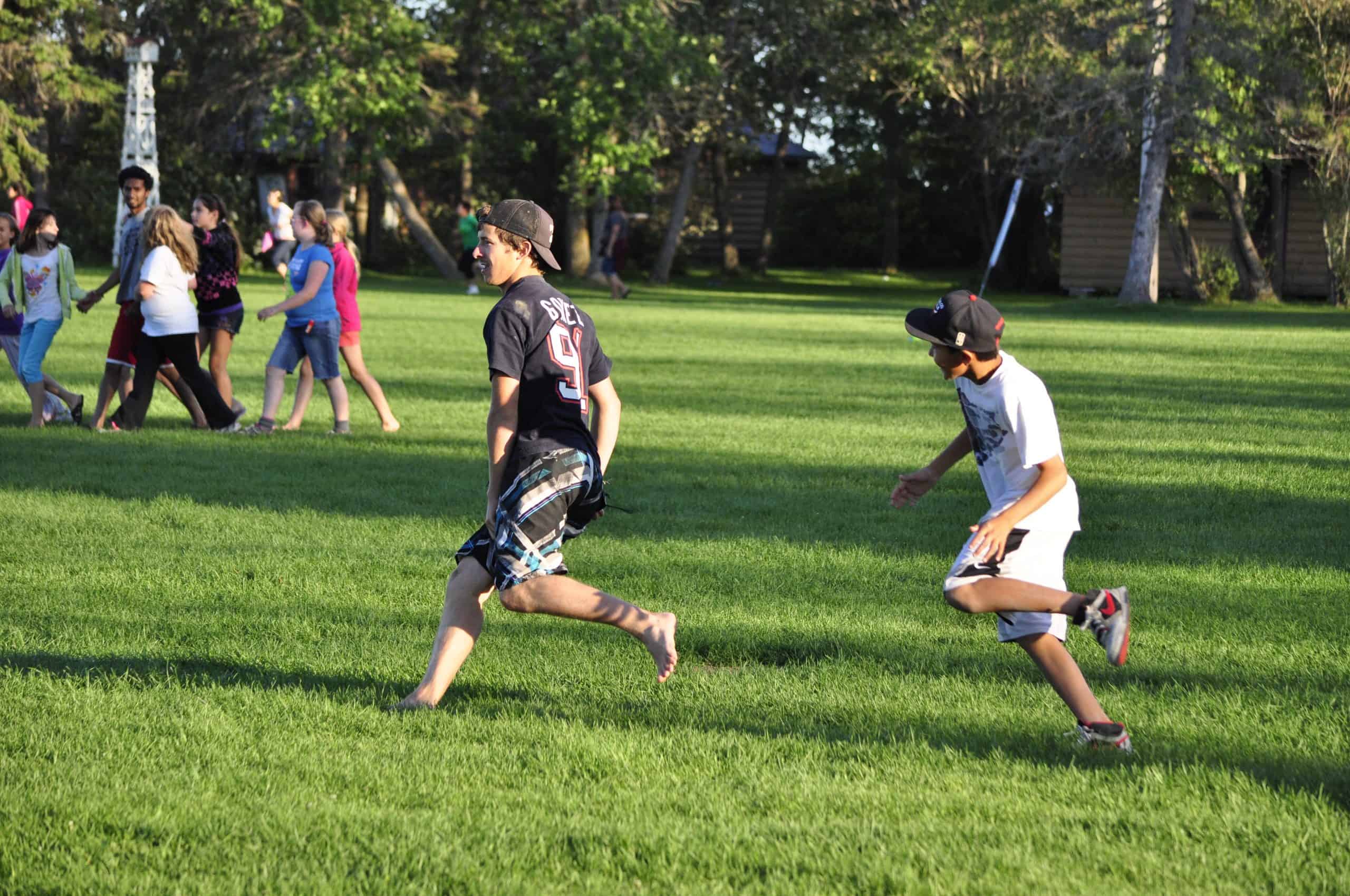 Open field at Camp Arnes with kids playing and running, natural outdoor scenery, ideal for summer camp activities, outdoor recreation, and youth camp experiences in Manitoba.